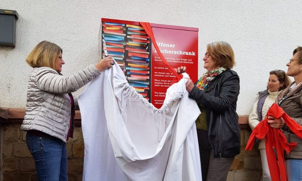 Auf dem Foto zum Bericht zur Eröffnung Bücherschrank sieht man Kathrin Schimmelpfennig (links) und Rosemarie Momberger (rechts) beim Enthüllen des Bücherschranks